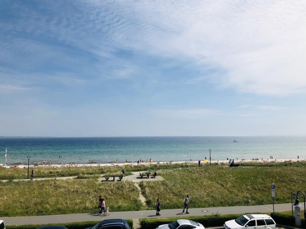 Strand mit grüner Dünenflanke und Wanderweg. Menschen genießen die Küstenlandschaft.
