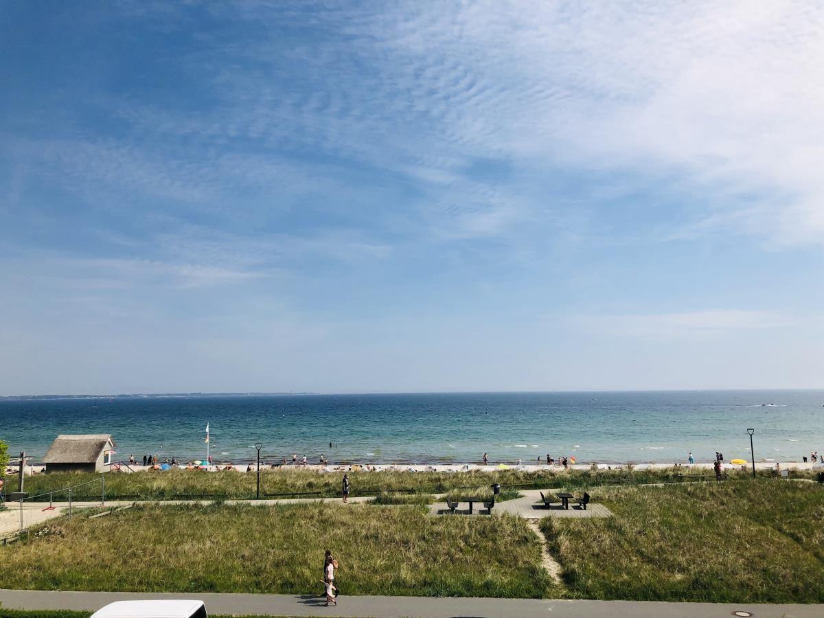 Meer und Strand mit Grünflächen und Besuchern unter blauem Himmel.