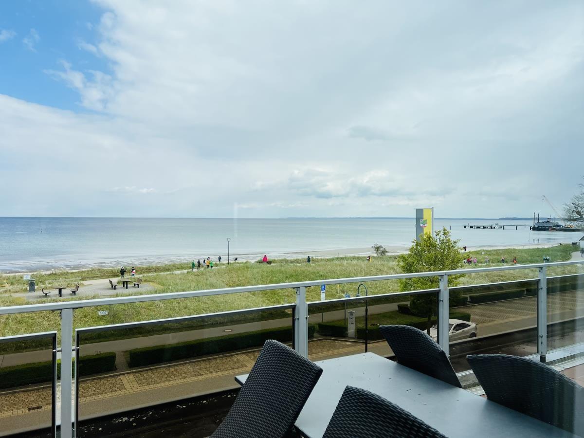 Terrasse mit Tisch und Stühlen bietet Blick auf Strand und Meer.