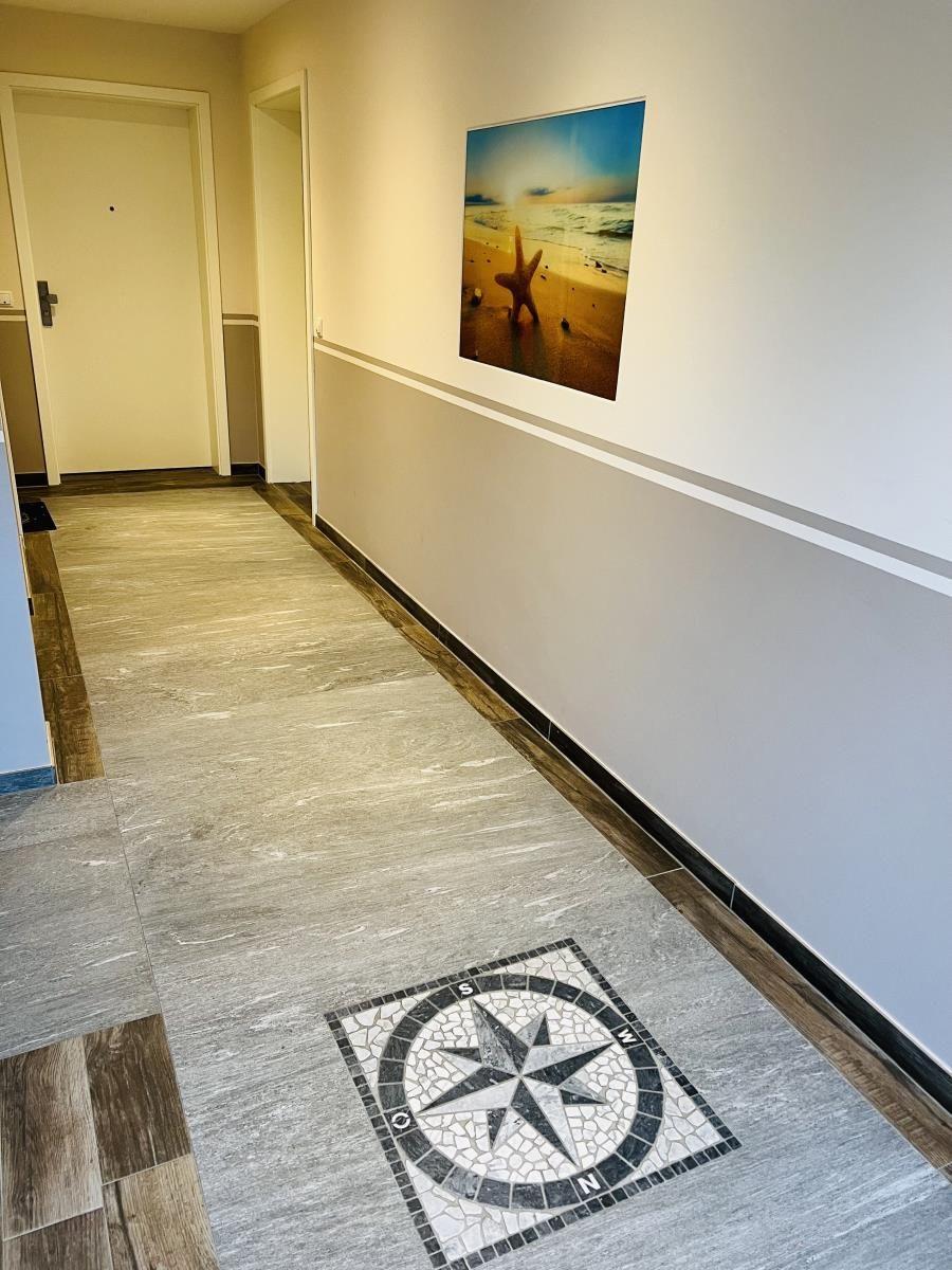Flur mit Mosaikkompass und Strandbild an der Wand.