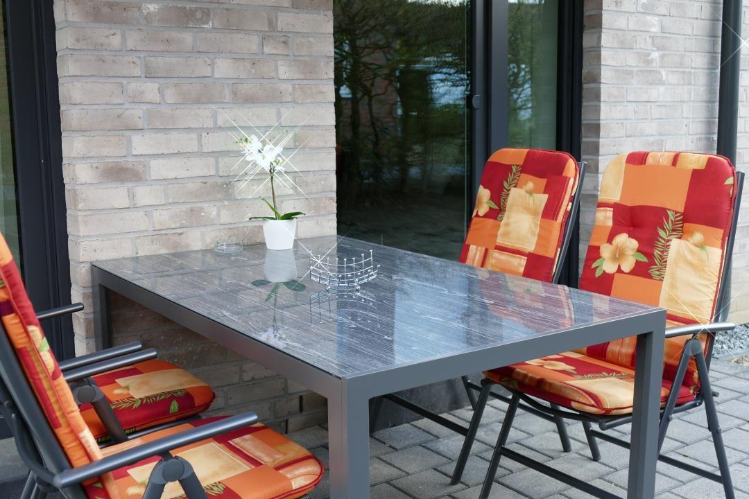 Terrasse mit Glas-tisch und Stühlen mit bunten Kissen.