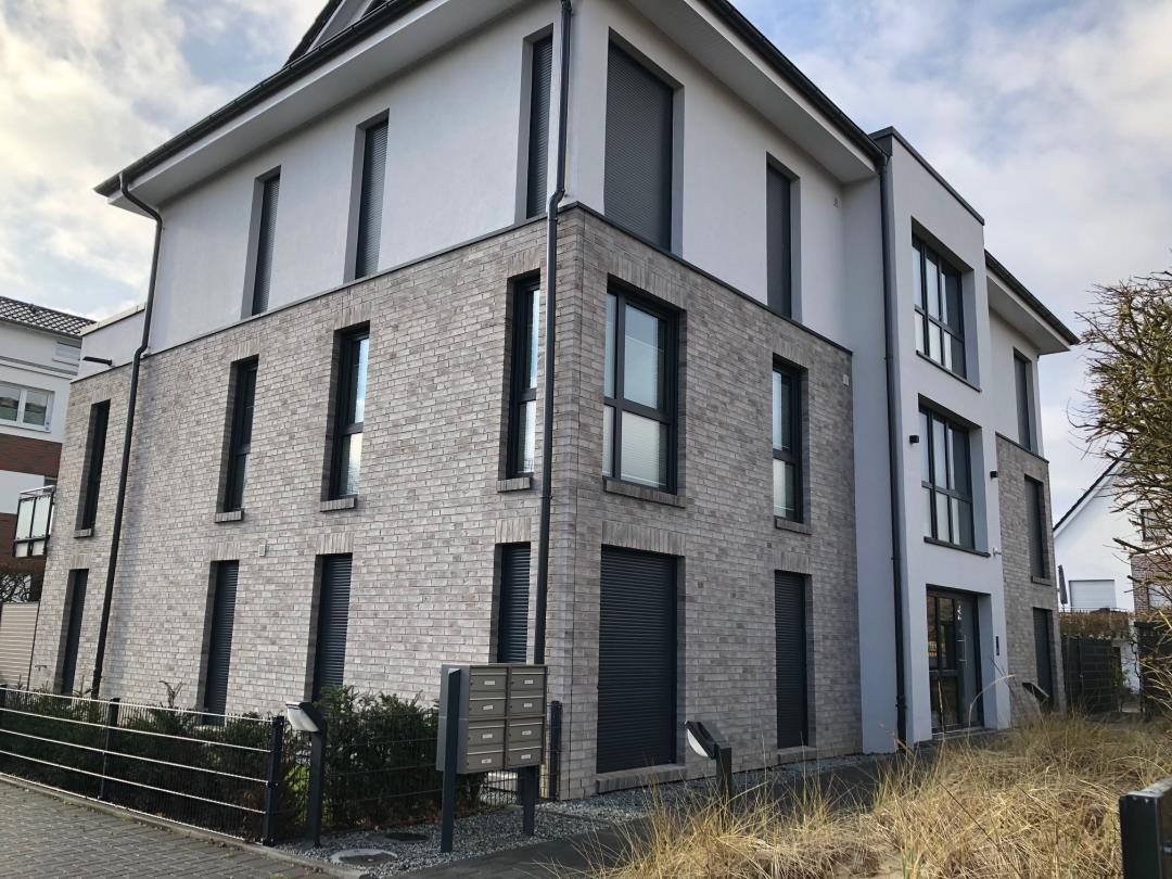 Modernes Haus mit grauem Backstein und weißen Fassadenbereichen. Große Fenster und dunkle Rollläden.