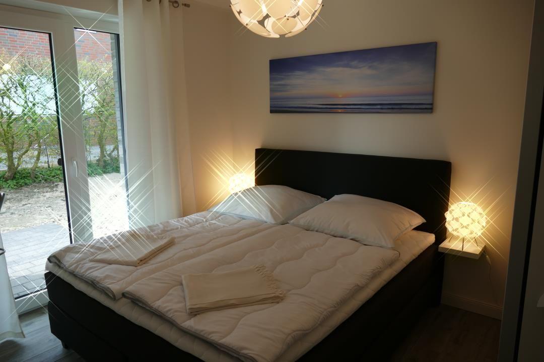 Schlafzimmer mit Bett, Wandbild und Türe zum Außenbereich.