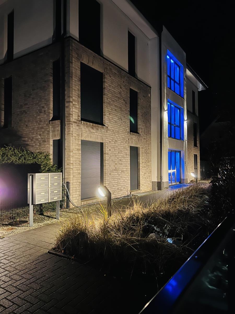 Moderne Hausfassade bei Nacht mit blau beleuchteten Fenstern und gepflastertem Weg.