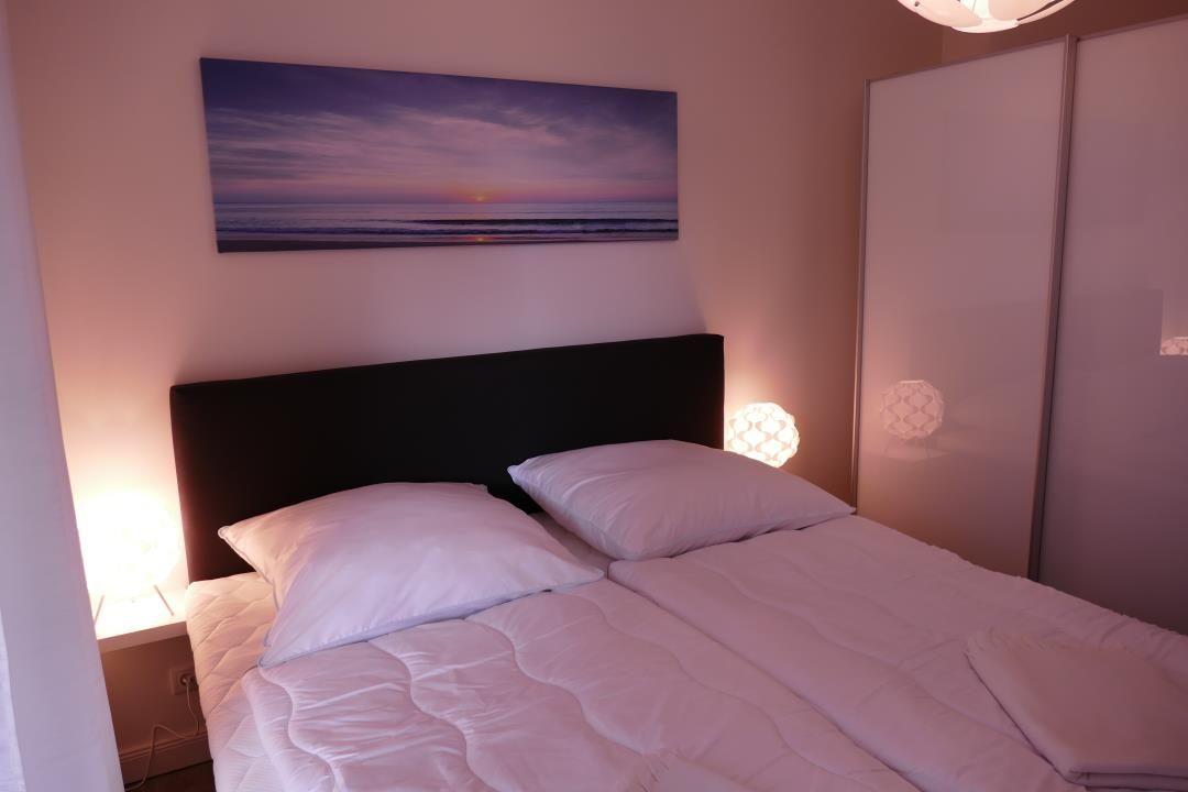 Schlafzimmer mit Doppelbett, Wandbild und zwei Nachttischen mit Lampen.