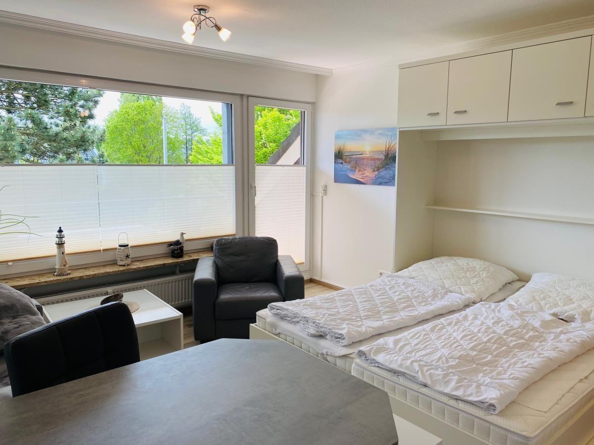 Schlafzimmer mit Doppelbett, Sitzgelegenheit und Fensterblick auf Grün.