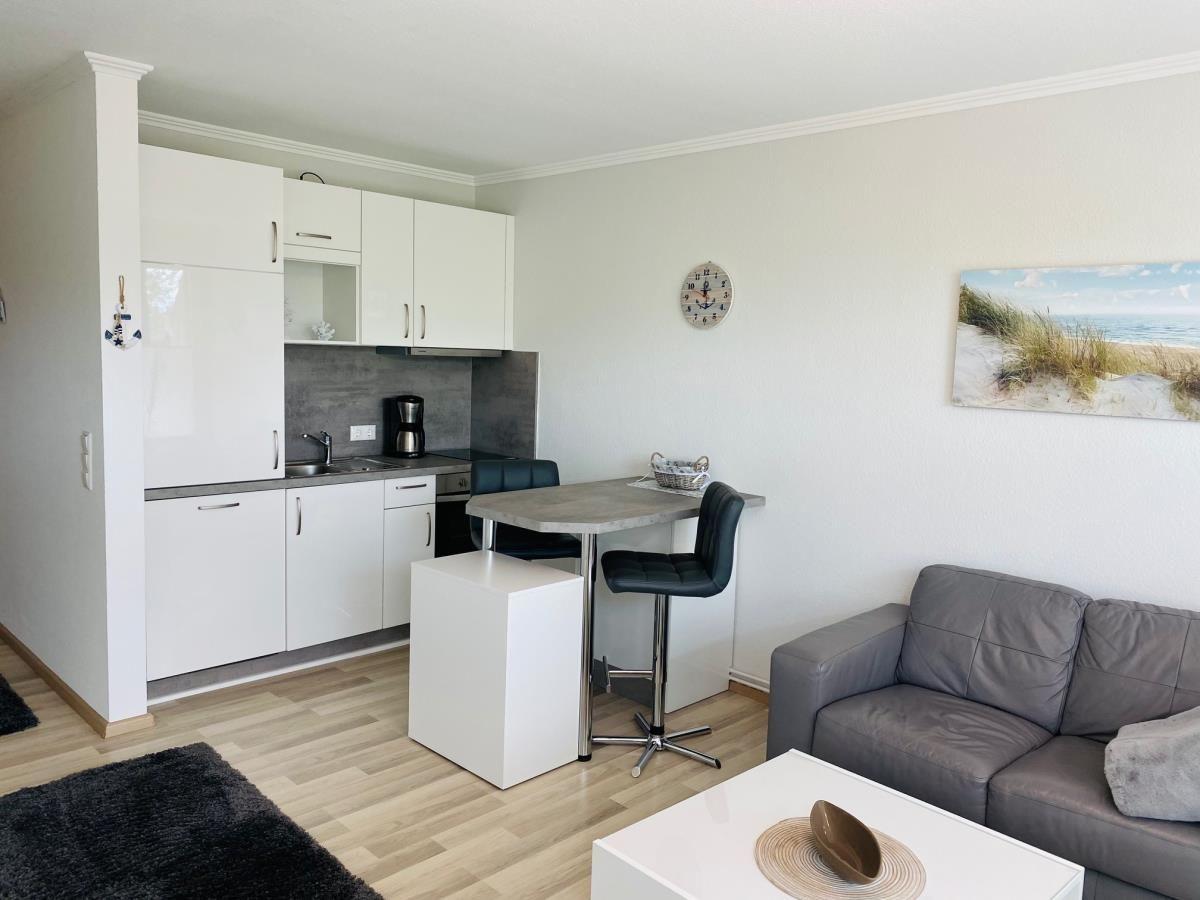 Wohnung mit Küche, Essbereich und Sofa. Wandbild und Uhr sichtbar.