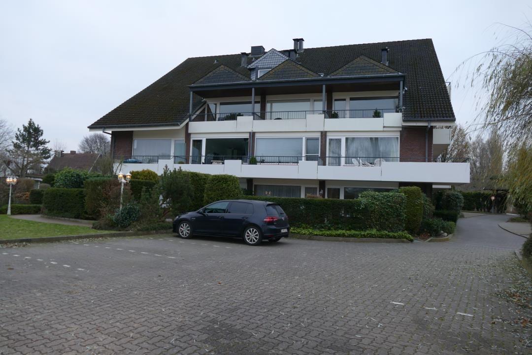 Modernes Mehrfamilienhaus mit Balkonen und gepflastertem Vorplatz. Ein dunkler Wagen steht vor dem Haus.