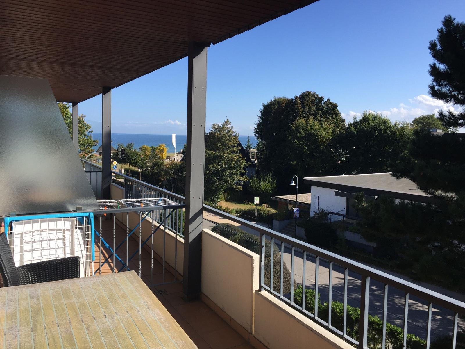 Terrasse mit Tisch und Stühlen, Blick auf Meer und Bäume.