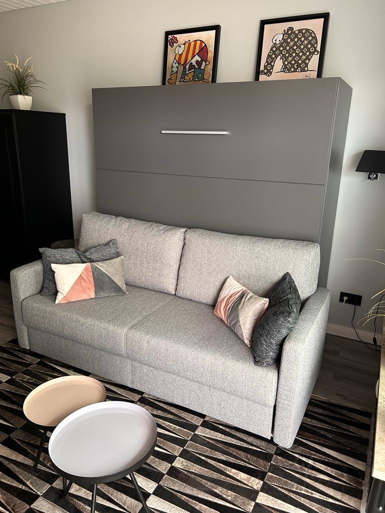 Gray sofa with cushions in front of wall with pictures and wall cabinet.