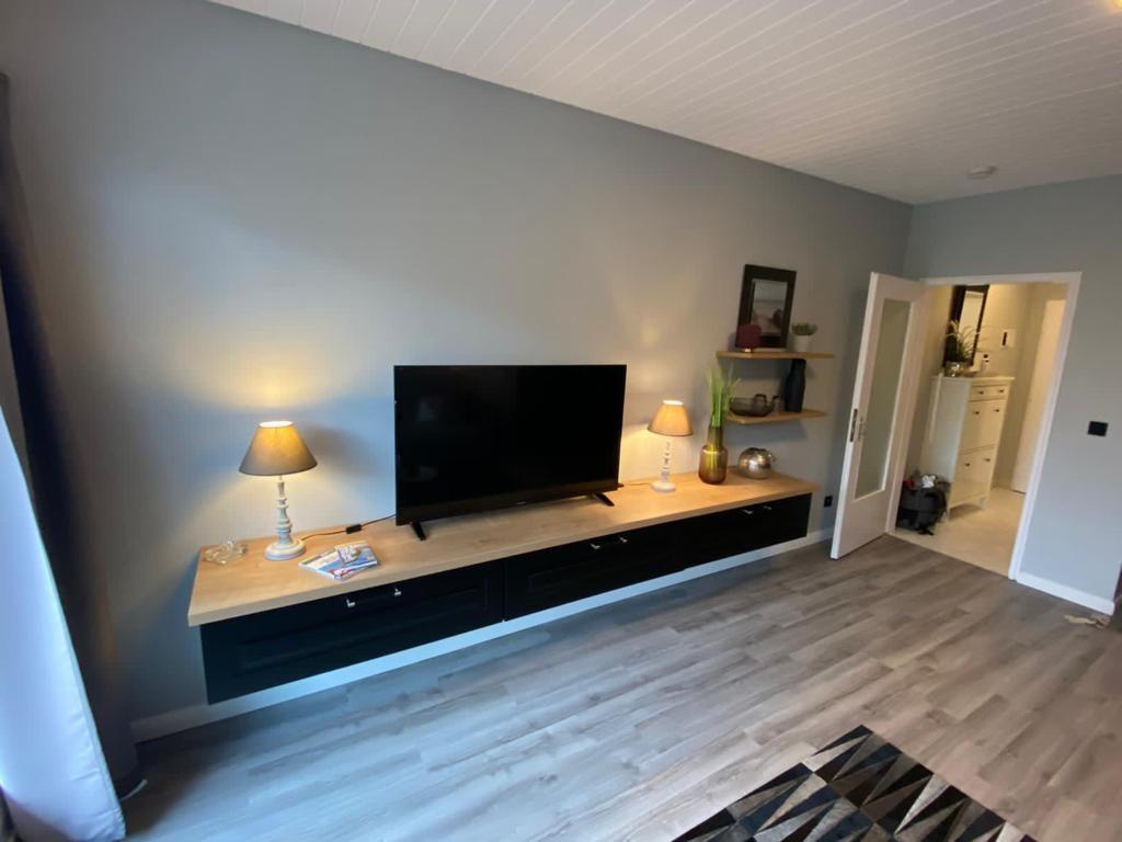 Living room with TV, wooden shelf, and lamps on baseboard.