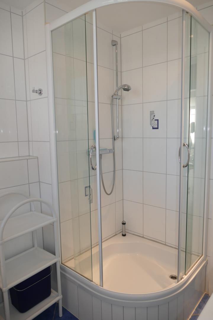 Duschkabine mit Glaswand und Duschbrause in weißer Badewanne