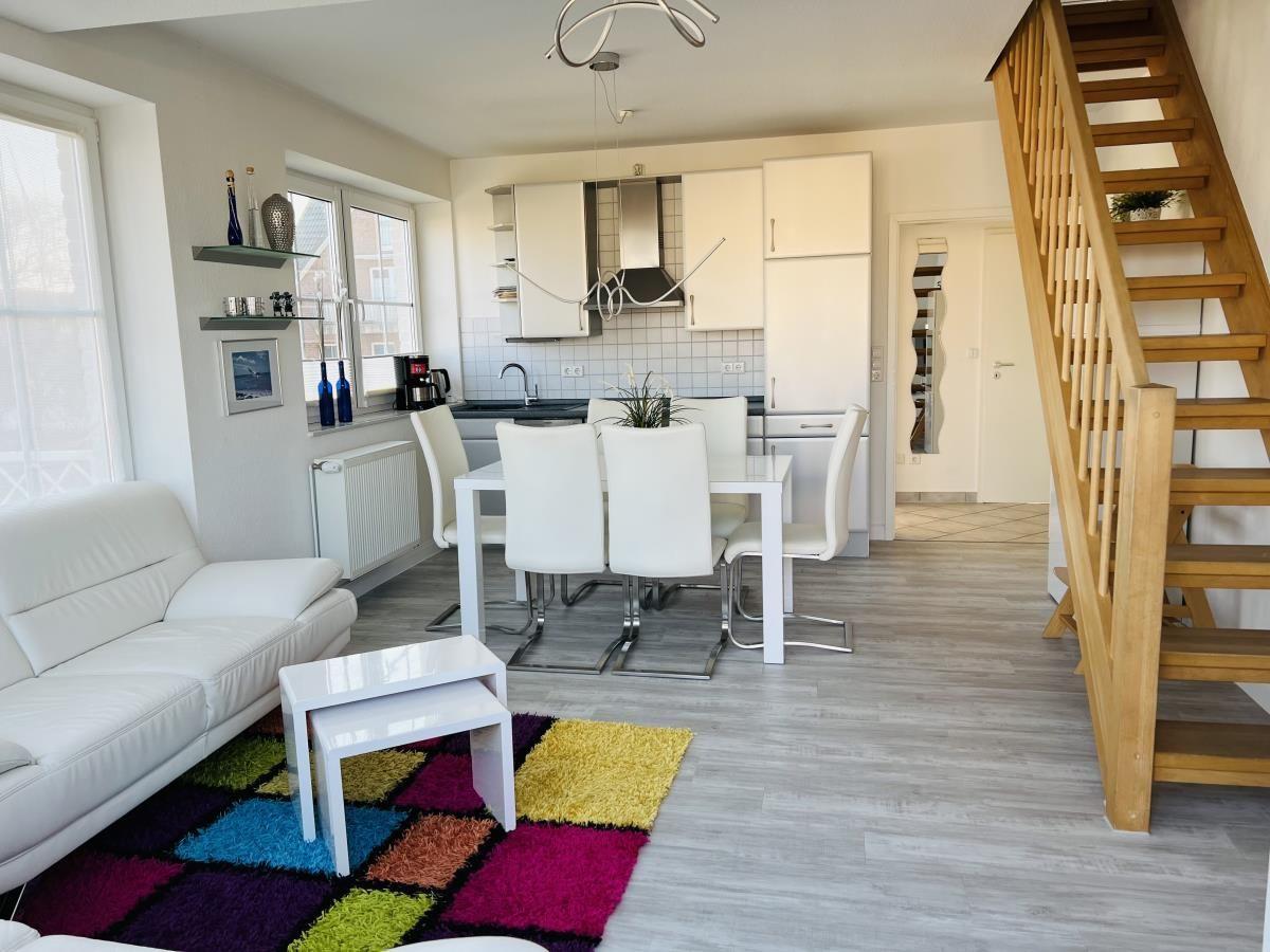 Wohn-Essbereich mit Küche, Sofa, Tisch und Holztreppe.