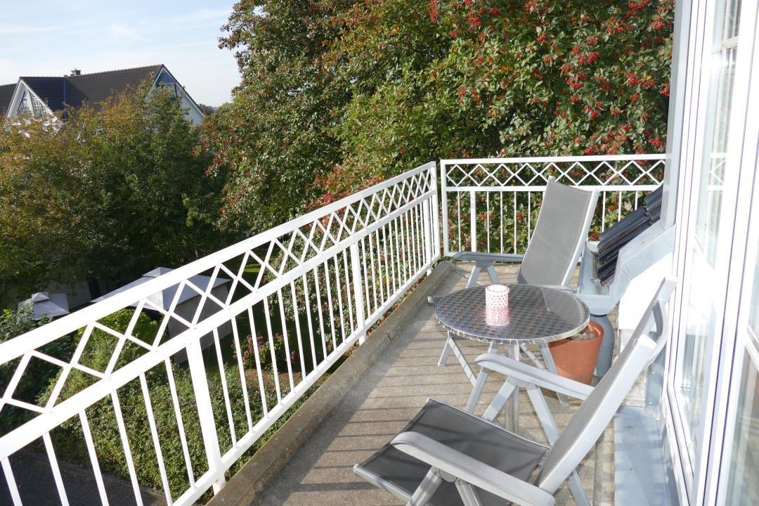 Balkon mit Tisch, Stühlen und Blick auf grüne Bäume.