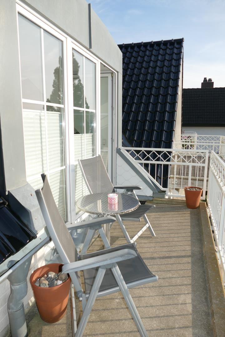 Terrasse mit Tisch und zwei Stühlen, Pflanzen und weißer Brüstung.