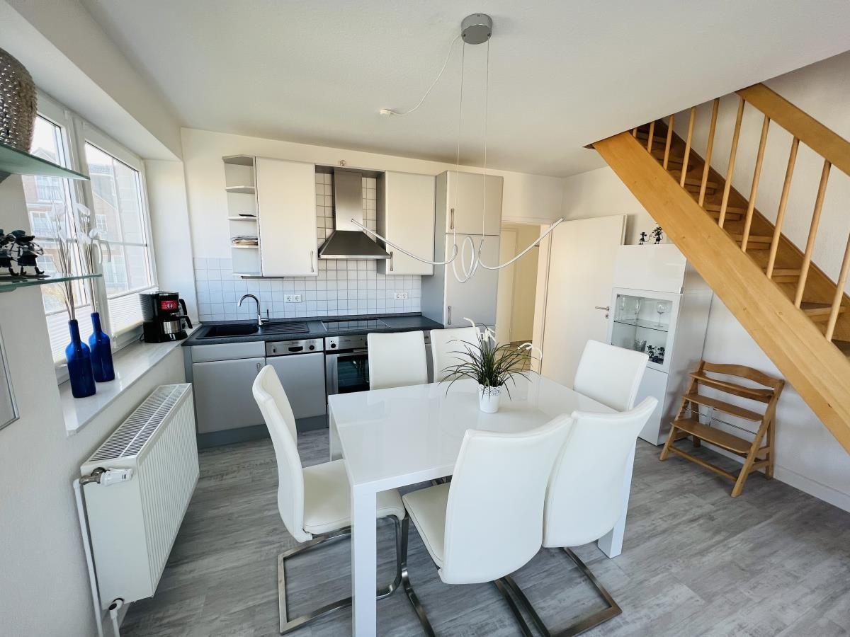 Küche und Essbereich mit weißem Tisch, Stühlen und Holztreppe.