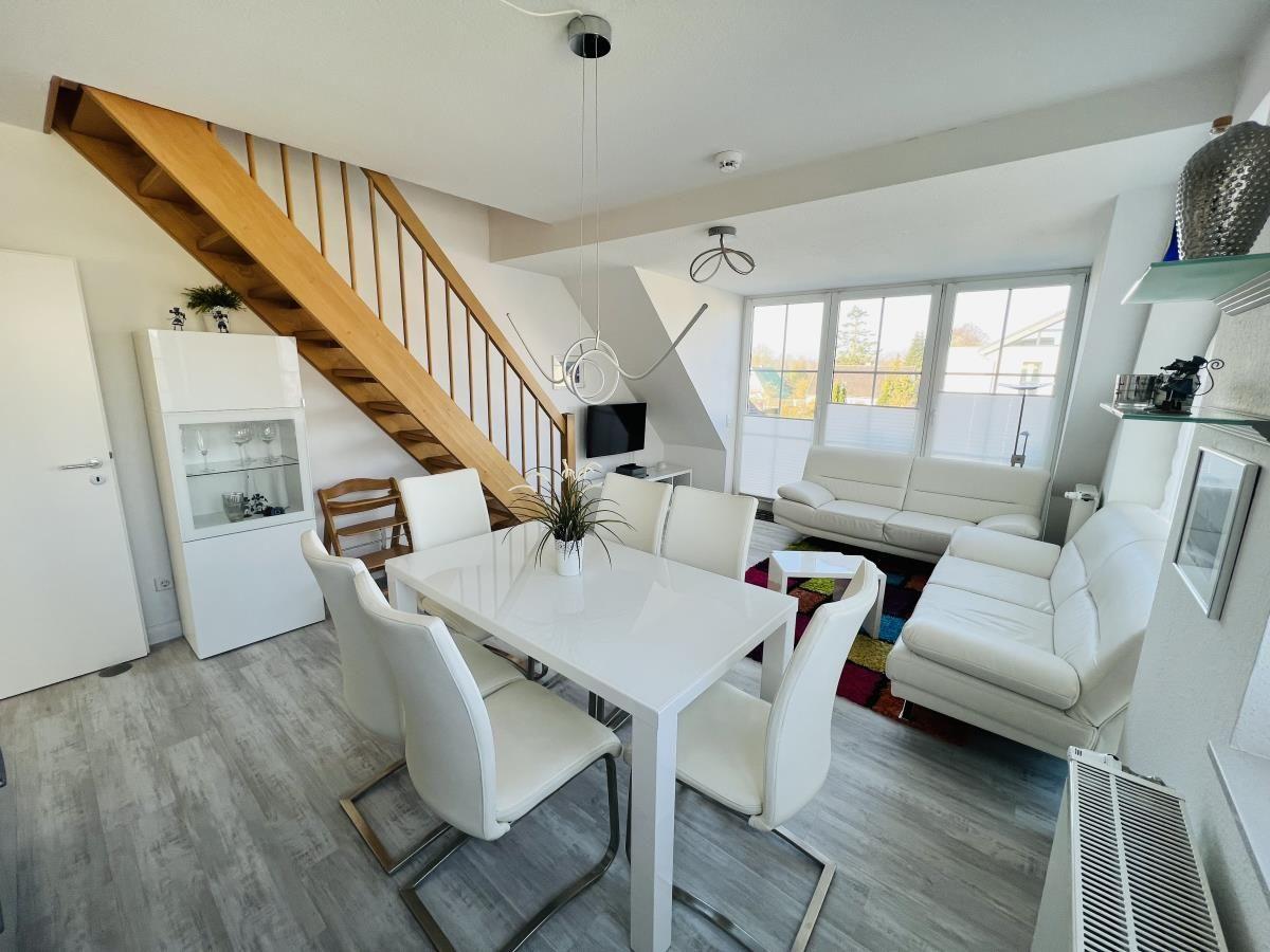 Wohn- und Essbereich mit weißem Sofa, Esstisch und Holztreppe.