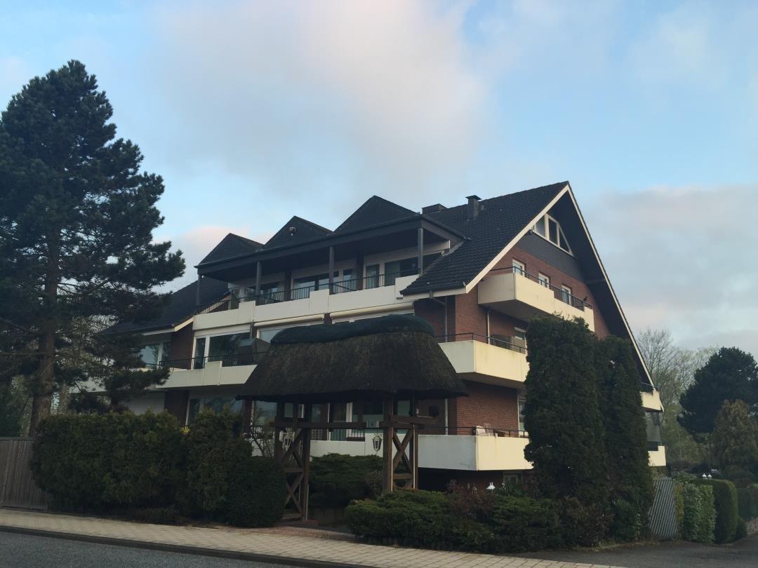 Mehrfamilienhaus mit Balkonen und Dachgauben. Vorhof mit strohgedecktem Tor.