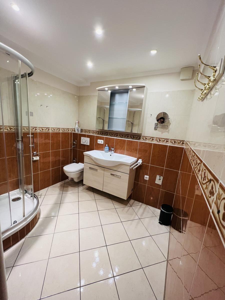 Badezimmer mit Dusche, Waschbecken und Toilette. Fliesenwand und Boden.
