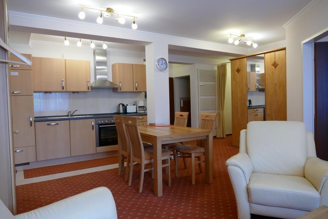 Küche mit Essbereich und Wohnzimmer mit weißen Sesseln und Holzmöbeln.