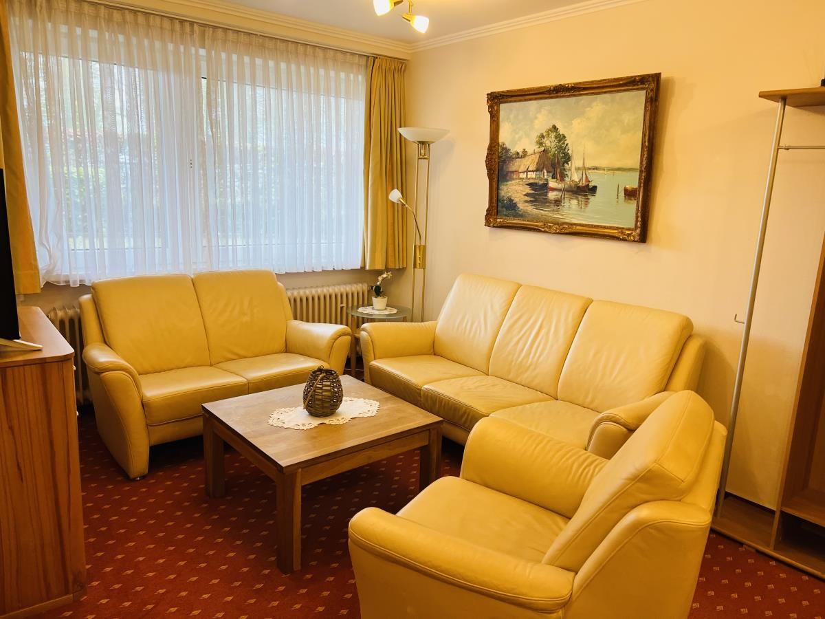 Wohnzimmer mit zwei Sofas, Sessel und Tisch. Wandbild und Fenster mit Vorhängen.
