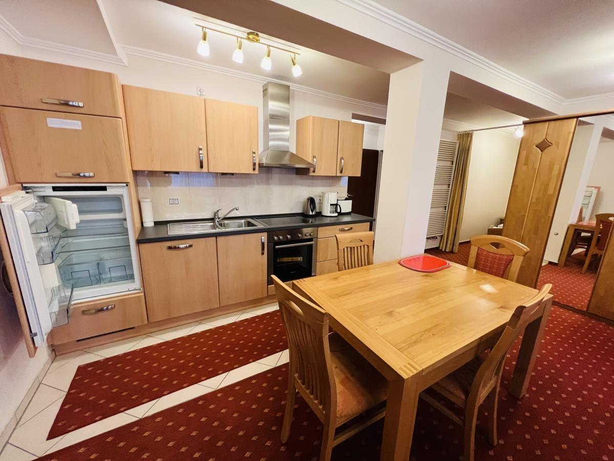 Küche mit Essbereich, Holztisch und Stühle. Kühlschrank offen. Teppichboden.