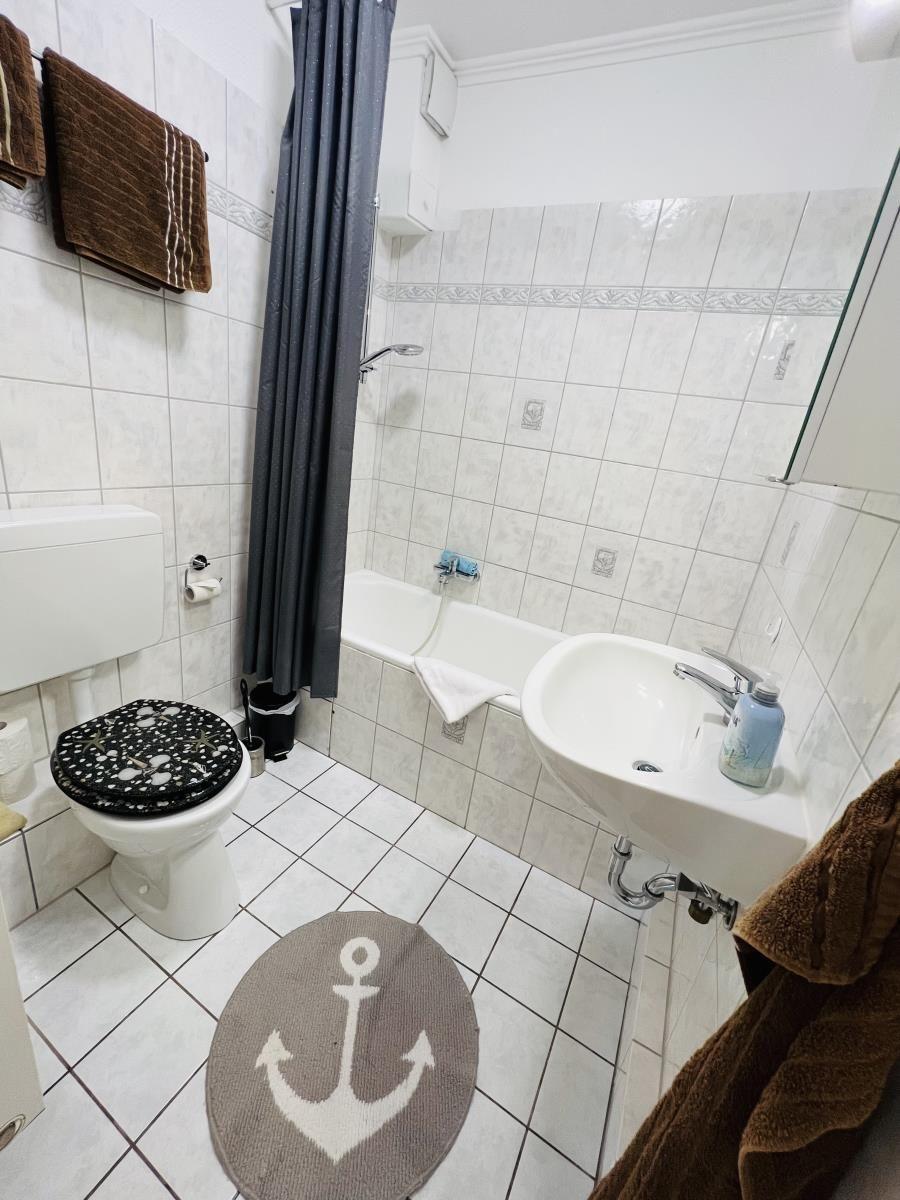 Badezimmer mit Badewanne, Toilette und Waschbecken. Boden- und Wandfliesen. Anker-Matte.