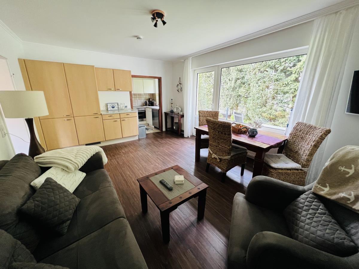 Wohnzimmer mit Essbereich, Küche und großem Fenster. Holzboden und wohnliche Einrichtung.
