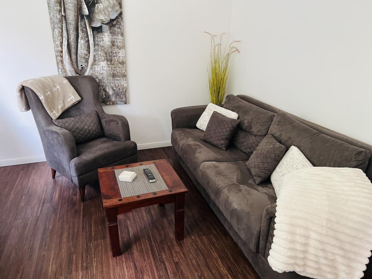Wohnzimmer mit Sofa, Sessel und Holztisch. Wandbild und Pflanze sind sichtbar.