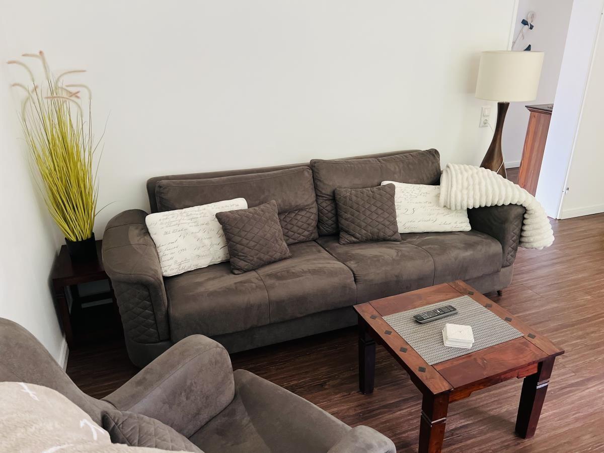 Ein Wohnzimmer mit braunem Sofa, Kissen und Holztisch.