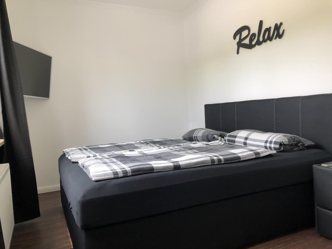 Schlafzimmer mit Bett, Wanddekoration und Fernseher.