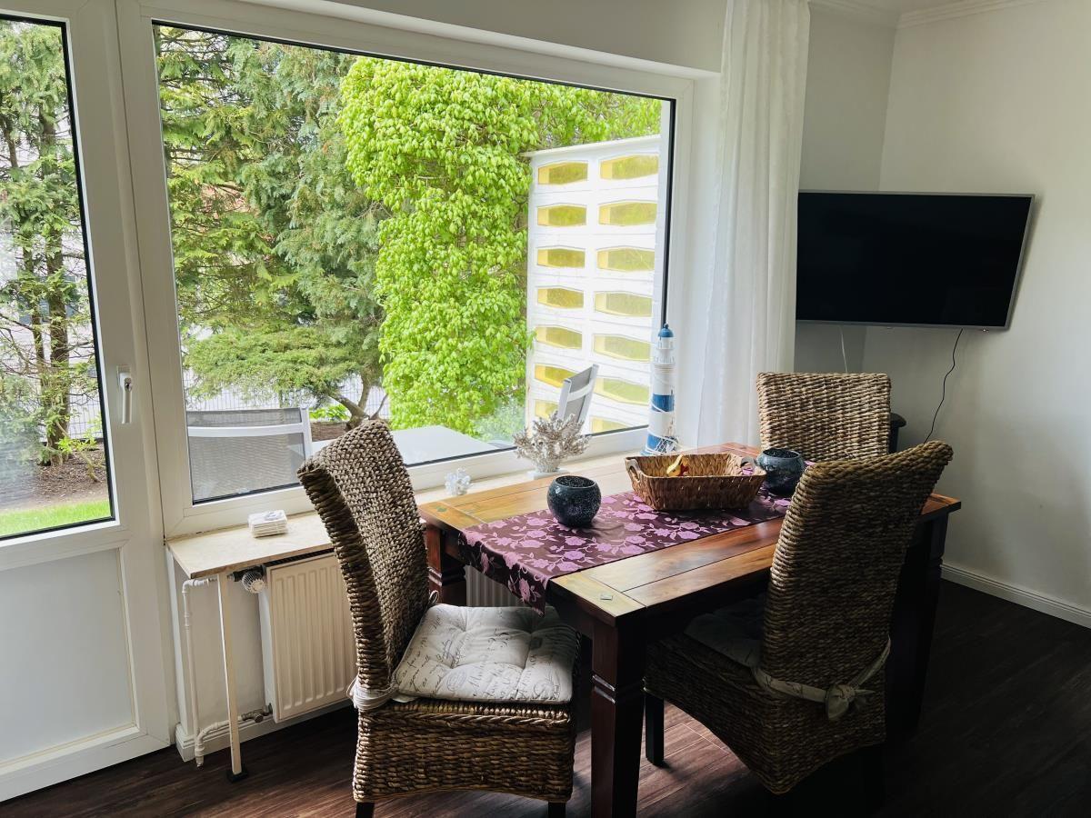 Esstisch mit vier Stühlen vor großem Fenster mit Blick auf Garten.