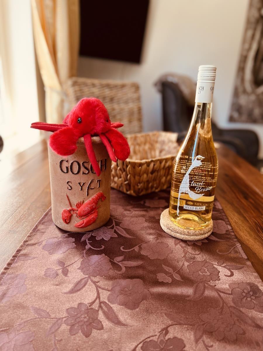 Auf Tisch steht eine Flasche Weißwein und ein roter Plüschkrabbe auf einem Keramikbecher.