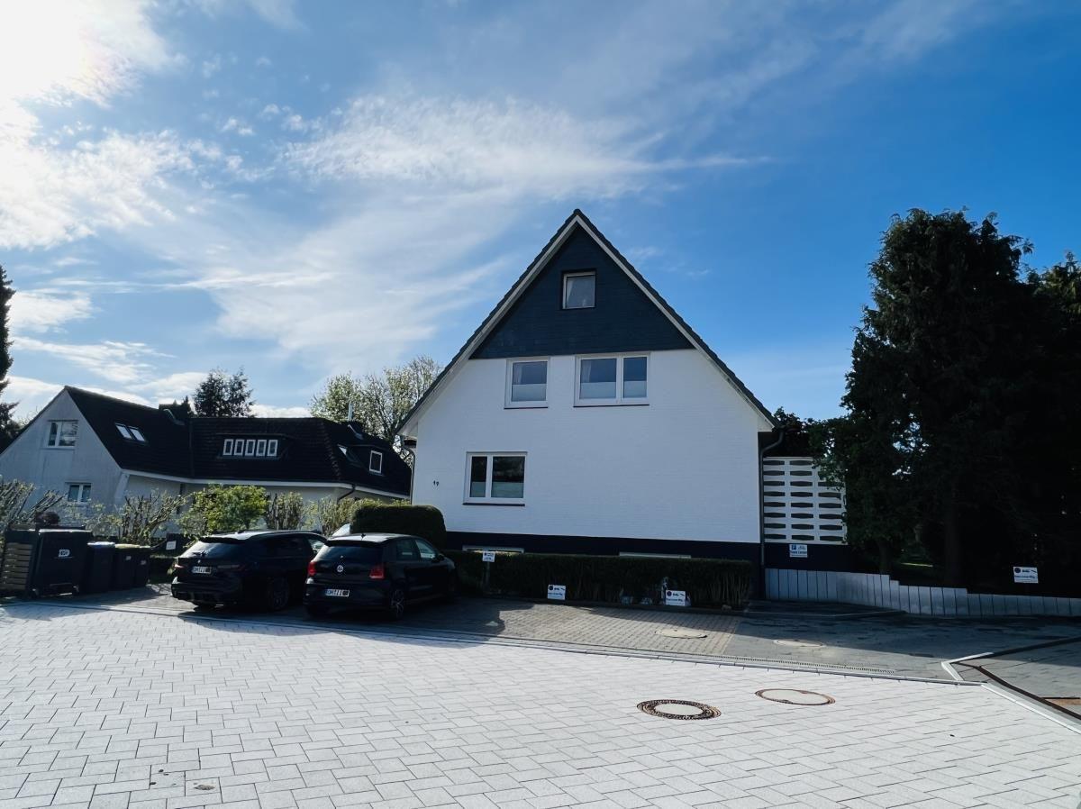 Modern house with white facade and black roof, paved forecourt with parked cars.