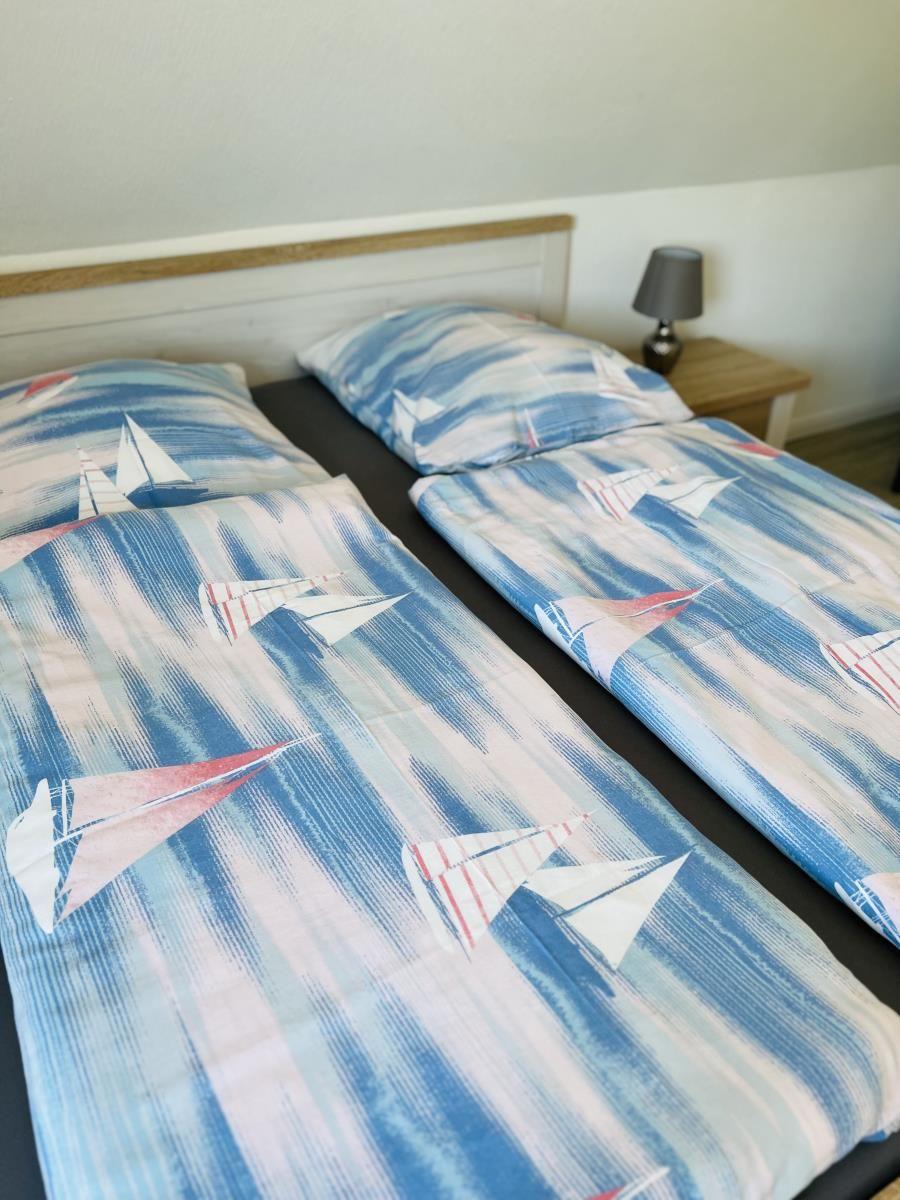 Two beds with sailboat-patterned bedding and a nightstand with a lamp.