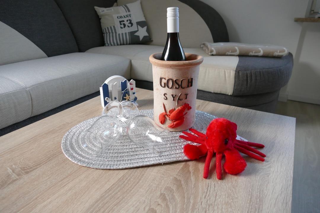 Table with wine cooler, glasses, and red plush toy in front of sofa.