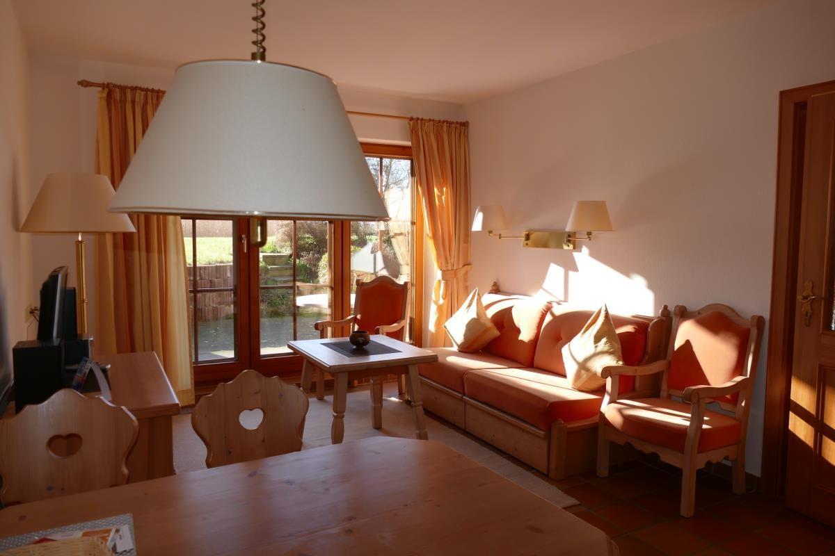 Wohnzimmer mit Sofa, Stühlen und Tisch. Durchgangstür und Fenster mit Vorhängen.