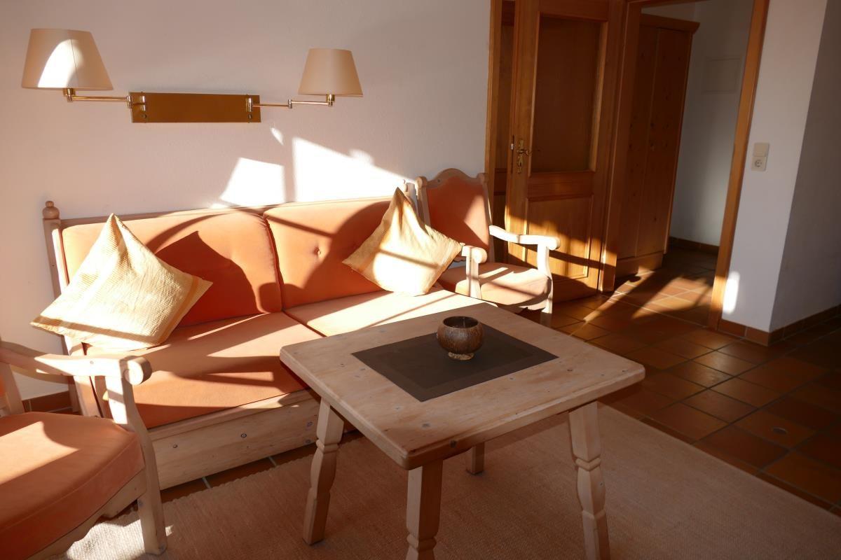 Wohnzimmer mit Sofa, Tisch und Lampen. Holztür und Fliesenboden sichtbar.