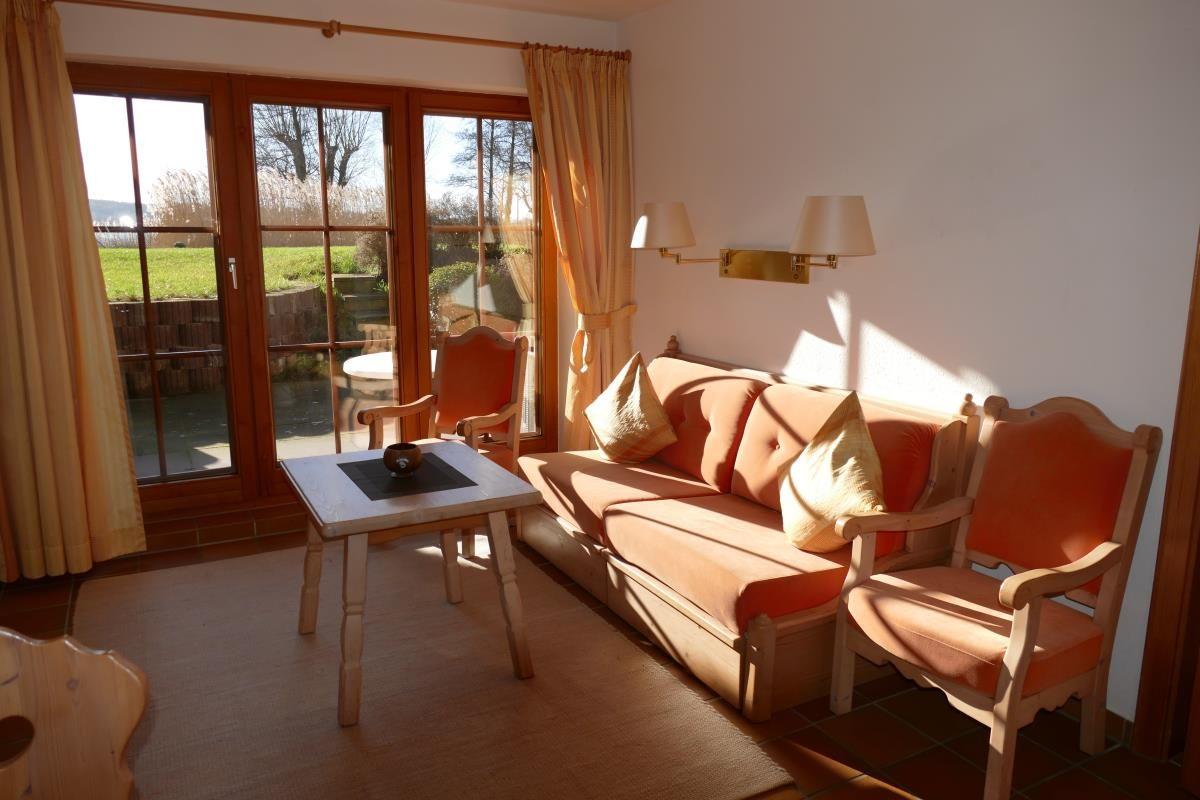 Wohnzimmer mit Sofa, zwei Stühlen und Tisch. Durchgangstür mit Blick auf Garten.