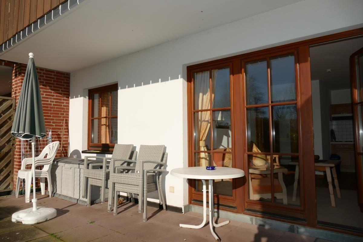 Terrasse mit Tisch, Stühlen und Sonnenschirm. Durchgehende Glasfront zur Küche.