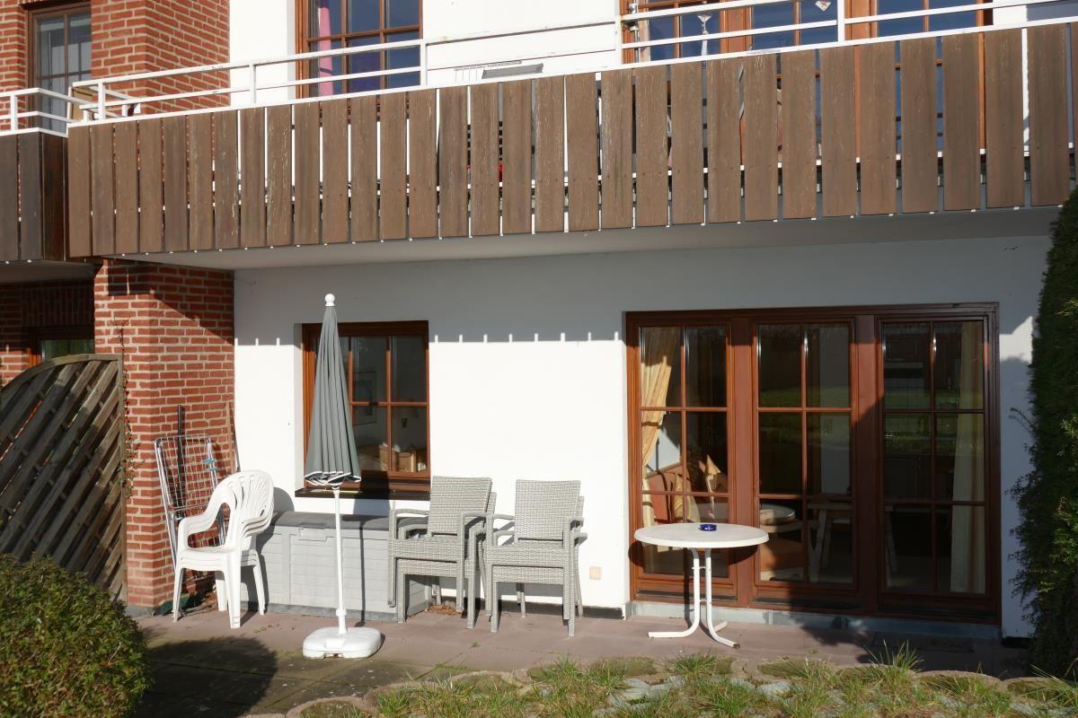 Terrasse mit Tisch, Stühlen und Sonnenschirm. Holzgeländer und Fenster sichtbar.