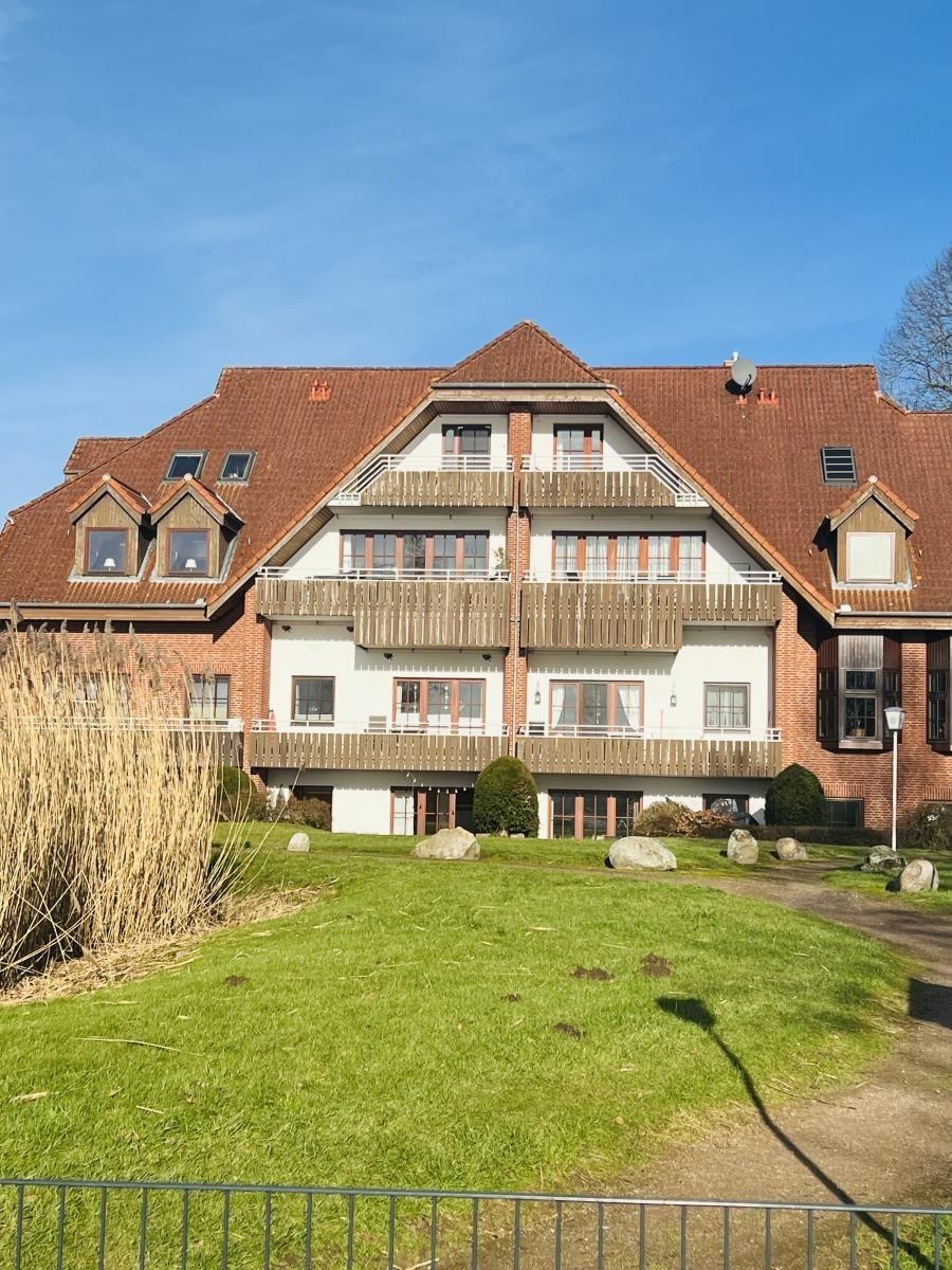 Haus mit mehreren Balkonen und rotem Dach, umgeben von Grünfläche und Steinen.