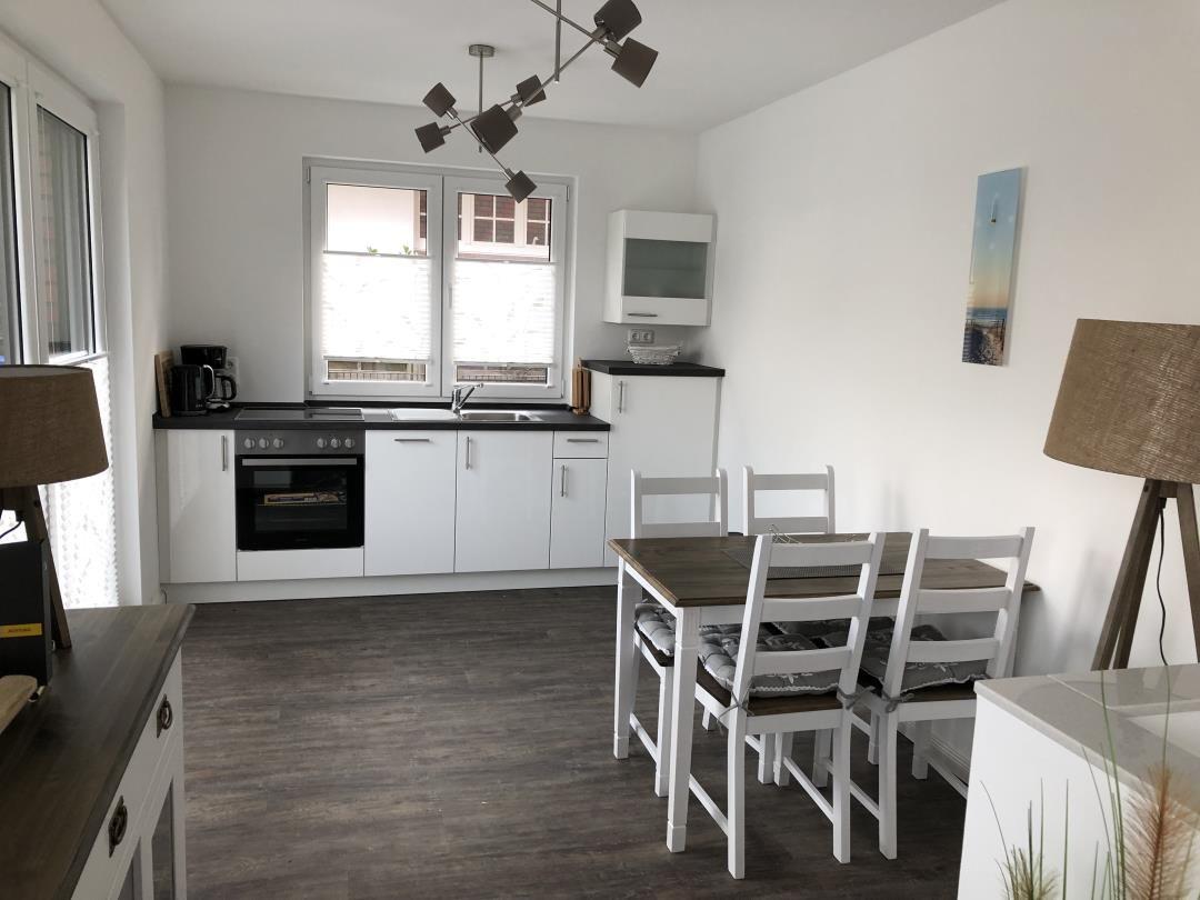 Küche mit Essbereich, weißer Einbauküche und Holztisch mit Stühlen.