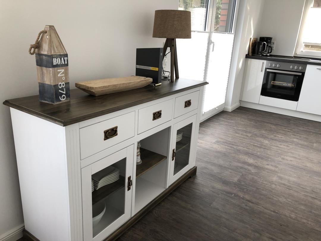Weißer Sideboard mit dunklem Holzoberflächen und Glasfronten, daneben Küche mit Backofen.