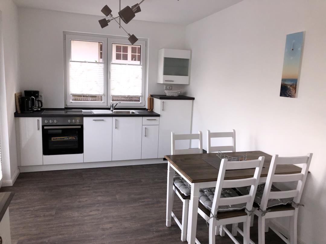 Küche mit Essbereich, weißer Arbeitsplatte und Holztisch mit Stühlen.