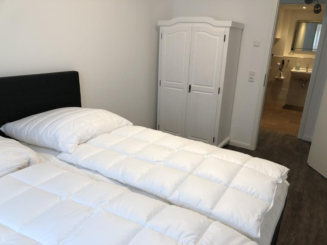 Schlafzimmer mit Bett, Kleiderschrank und Blick in die Badewanne.