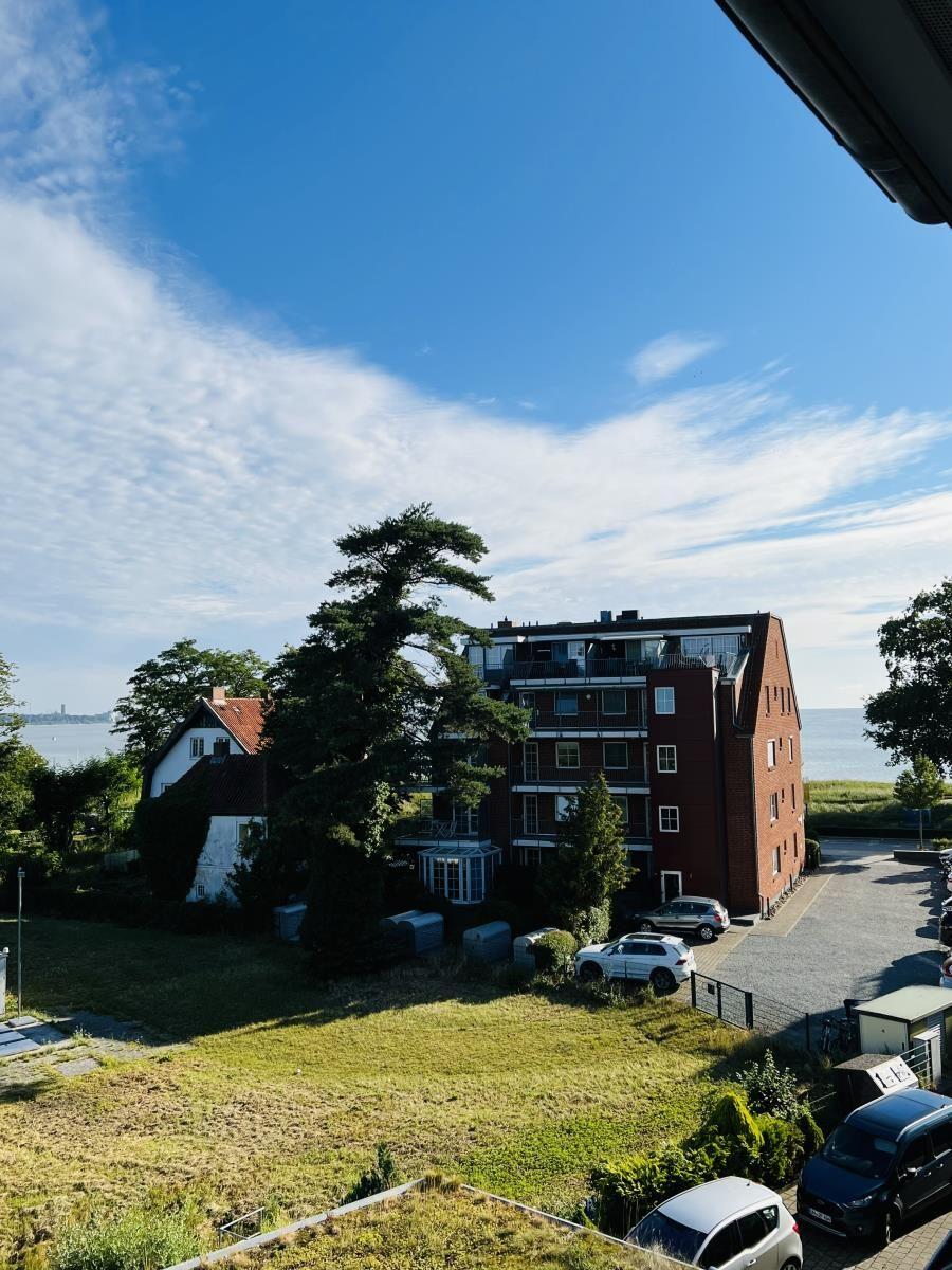 Red building with balconies, surrounded by green areas and a lake.