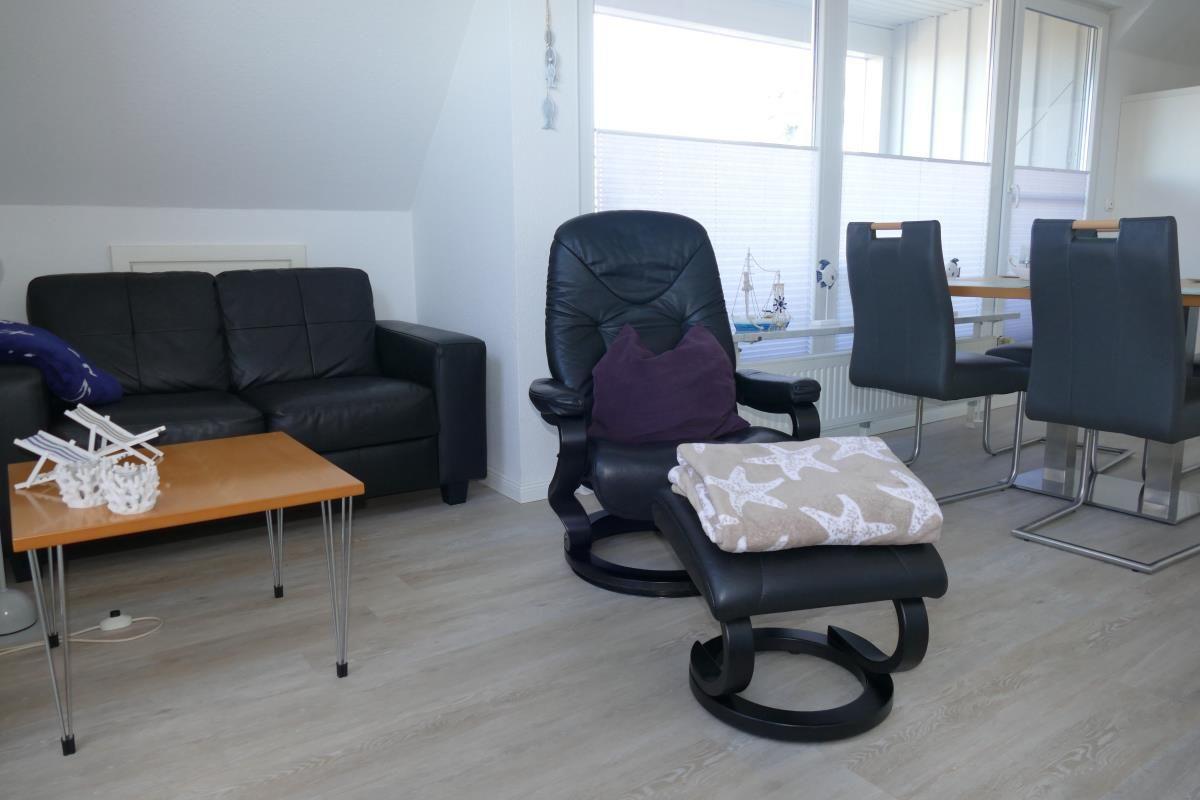 Living room with sofa, recliner, and dining table. Wooden floor and large windows.