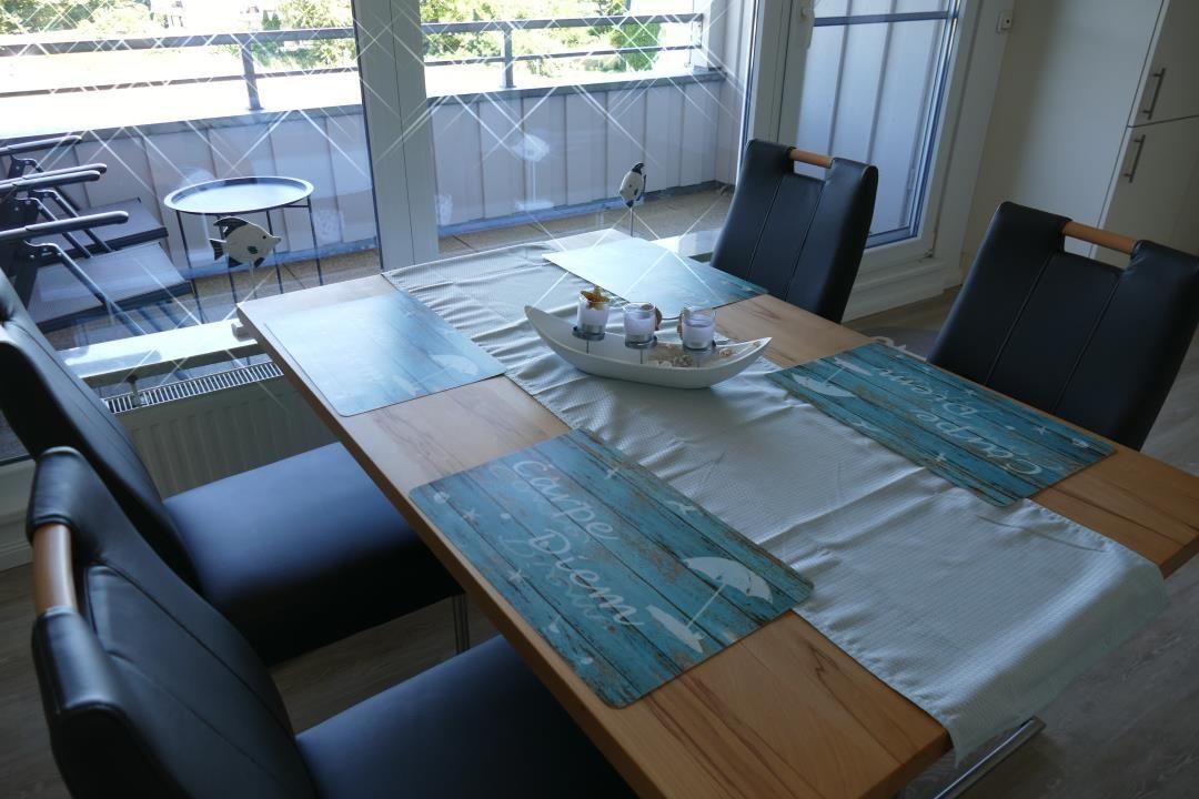 Dining table with four chairs and blue placemats near window with balcony view.