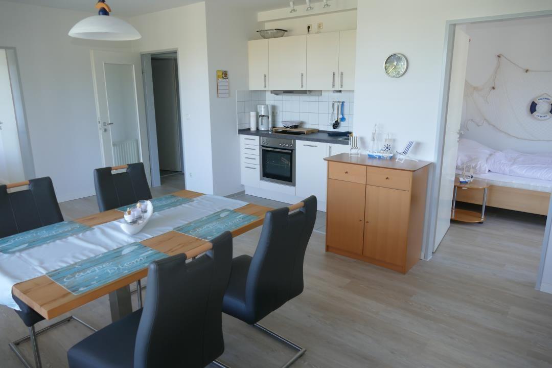 Dining room with table, chairs, and kitchen area. Bedroom with bed visible.